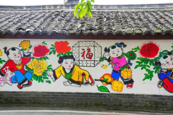 四川德阳有个喜庆的古村落，家家户户的墙上画着年画，色彩很...